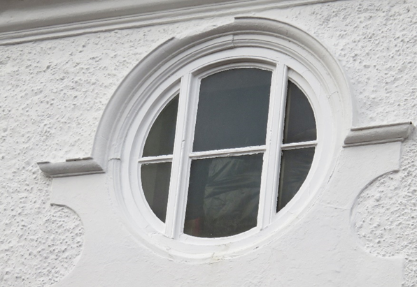 Rundes Fenster in einer älteren Fassade mit Sprossen in Form eines Gitters