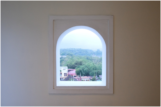 Rundbogenfenster mit Blick auf B&auml;ume sowie D&auml;cher eines Wohngebiets