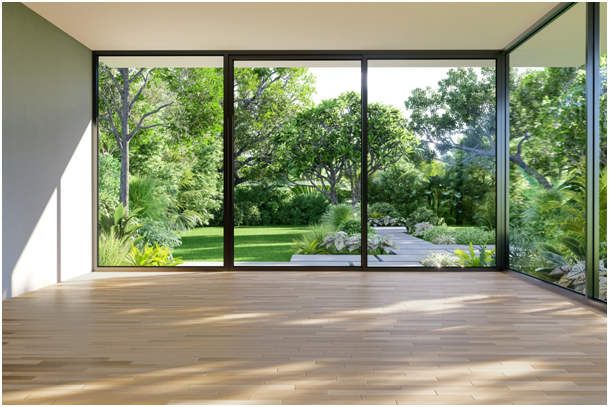 Leerer Raum mit bodentiefen Glasfronten und Blick auf einen gepflegten Garten mit Bäumen und Rasenfläche.